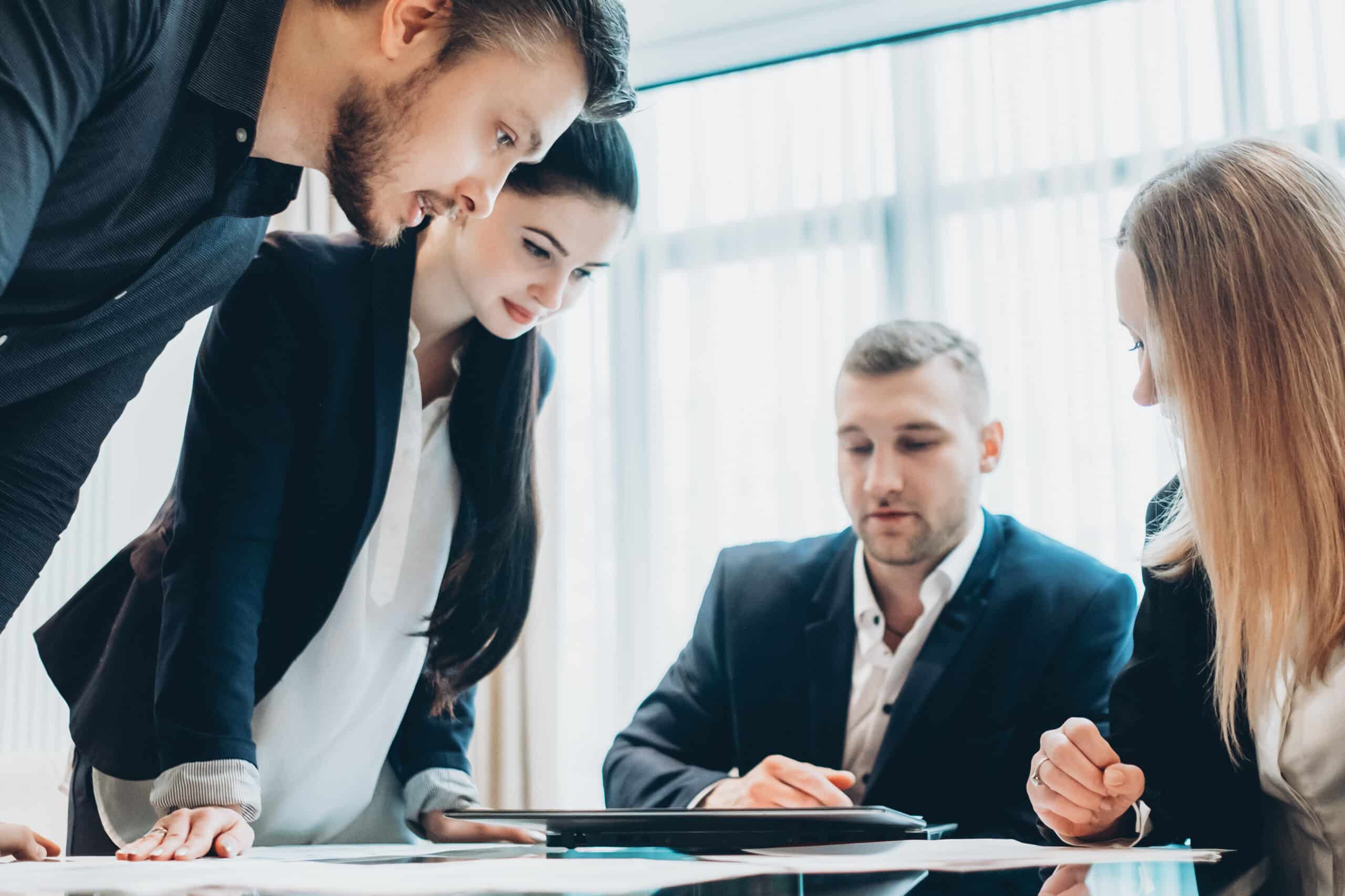 business people gather around conference table and collaborate while examining laptop screen
