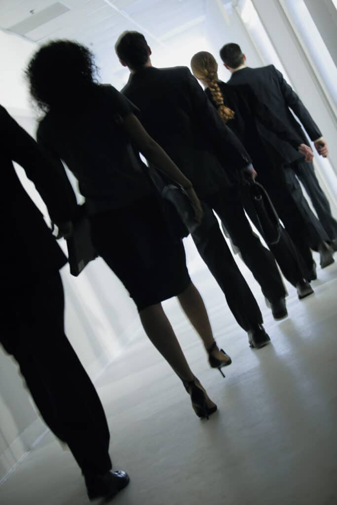 View from behind as team of financial analysts proceeds down a walkway in a commercial office building.